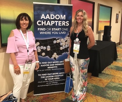 Kathy and Betsy standing either side of a large banner promoting AADOM
